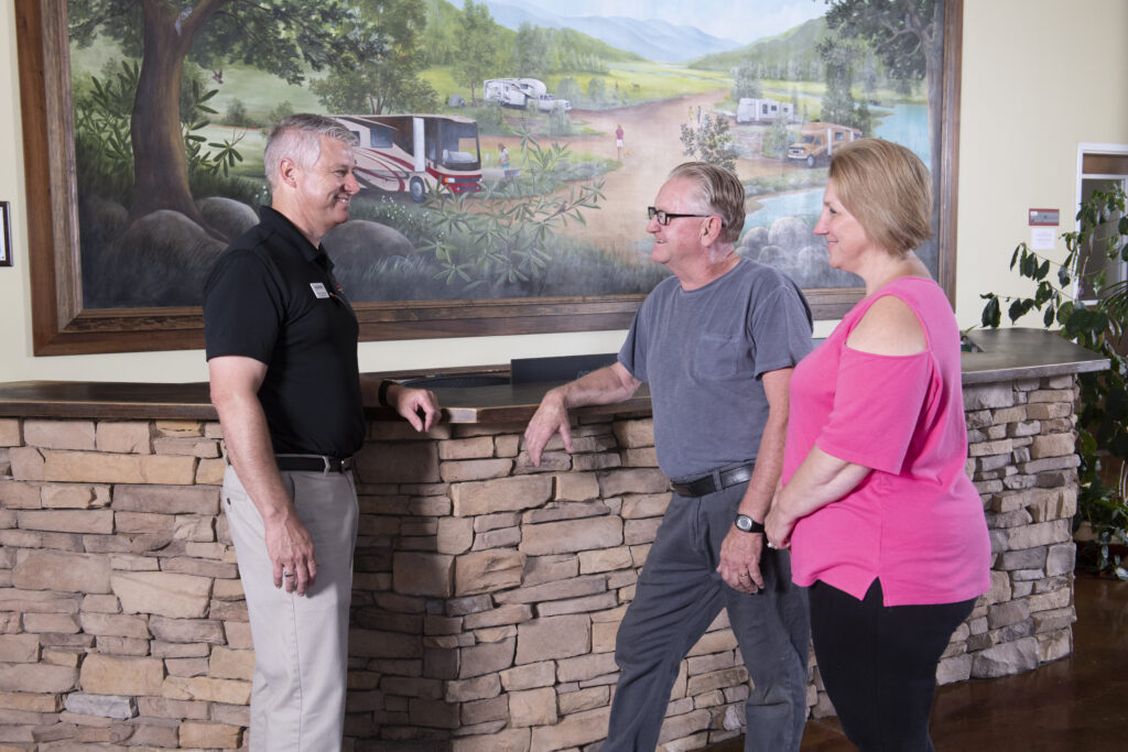 Smiling couple discussing selling their RV to a salesperson inside of an RV dealership.